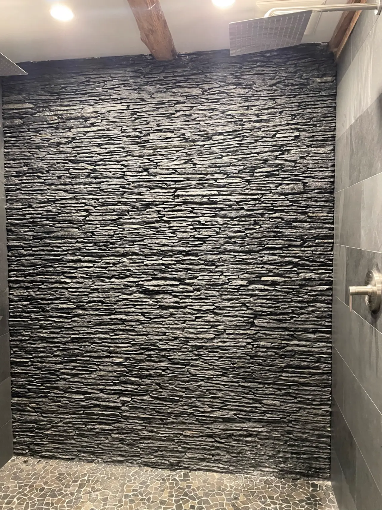 Floor-to-ceiling stacked black slate stone veneer accent wall inside a tiled walk-in shower