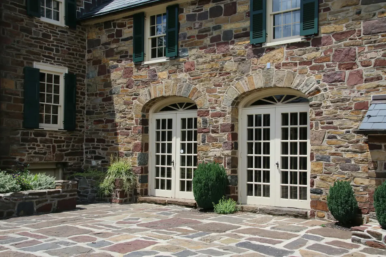 Hand-laid natural stone façade with arched French doors and flagstone patio — Legacy Mason Contractors project in Fairfield County, CT
